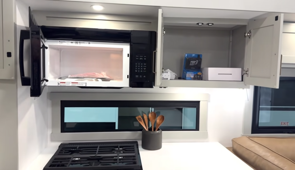 RV kitchen with open microwave and overhead storage cabinets above gas cooktop