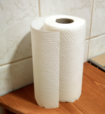 White roll of paper towels standing upright on a wooden countertop against a tiled backsplash, showing textured absorbent sheets ready for kitchen or RV cleanup.