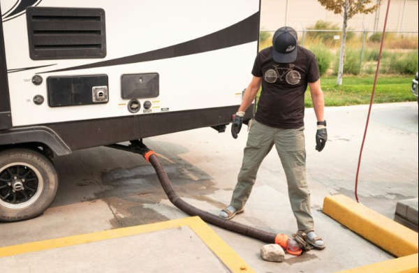 Man emptying an RV black tank at a dump station, wearing gloves while connecting a sewer hose to the RV’s waste outlet for proper wastewater disposal.
