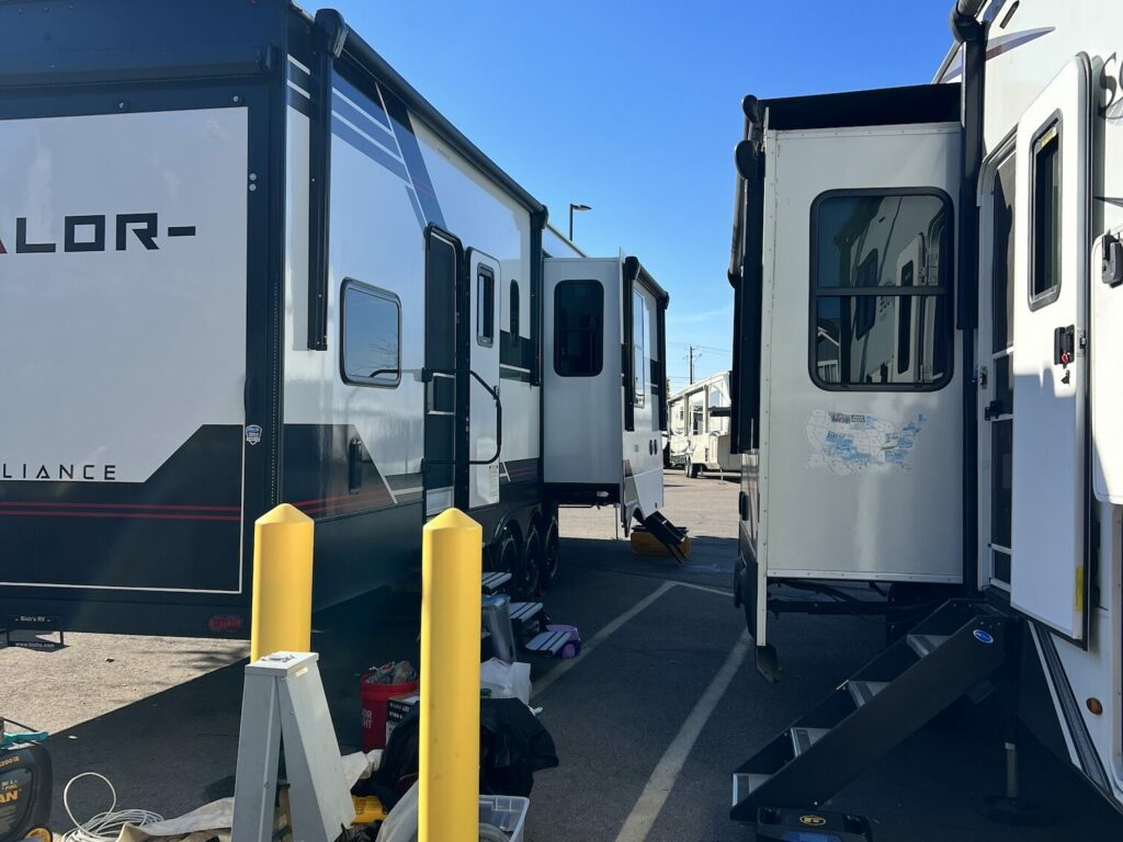 Multiple travel trailers with slide-outs extended parked closely together on an RV lot.