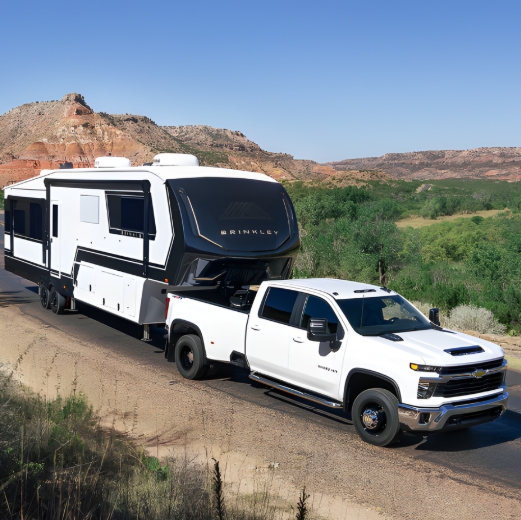 Pickup truck towing a Brinkley fifth wheel RV through a scenic desert landscape with mountains in the background.