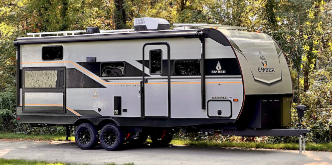 Ember travel trailer parked in a wooded campsite, featuring off-road tires and rugged exterior design.
