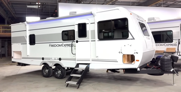Coachmen Freedom Express travel trailer with slide-out and entry steps displayed inside an RV showroom.