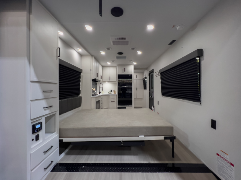 Toy hauler travel trailer interior with drop-down bed in garage area and kitchen visible toward the front of the RV.