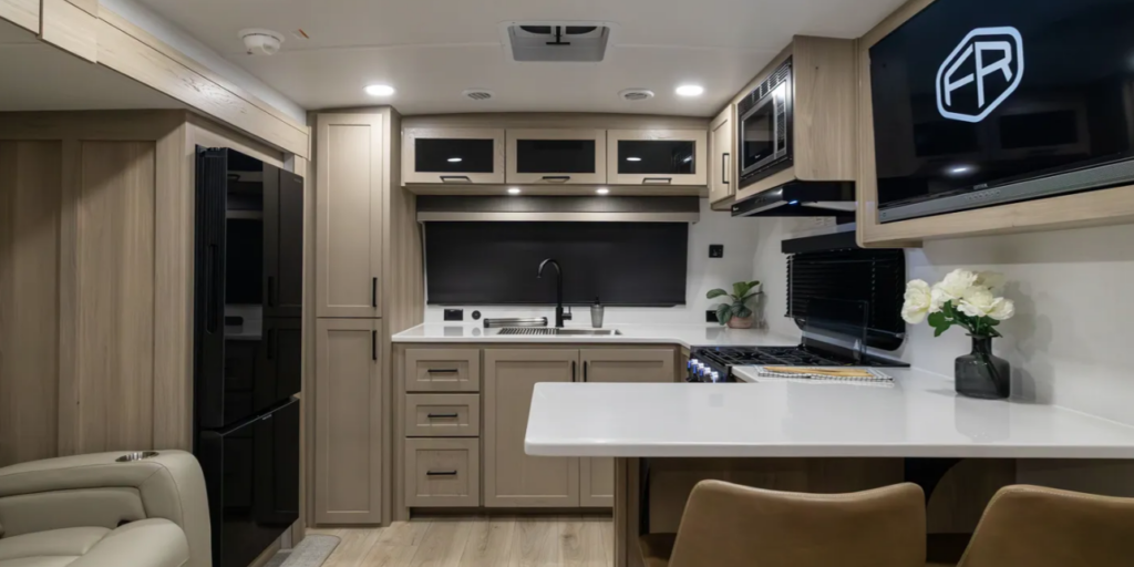 Rockwood travel trailer kitchen with large refrigerator, bar-style counter seating, microwave, and modern cabinetry.