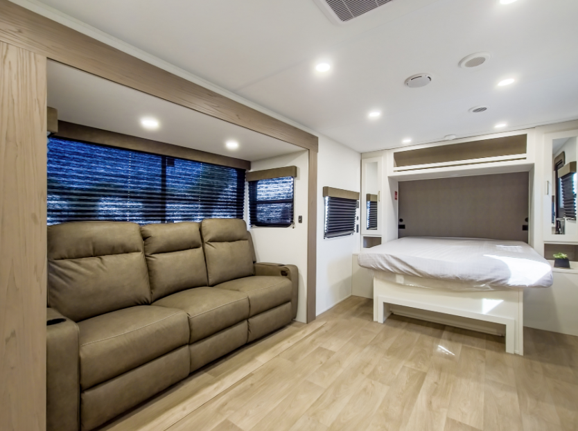 Travel trailer interior with sofa seating and rear queen bed in an open-concept RV living space.