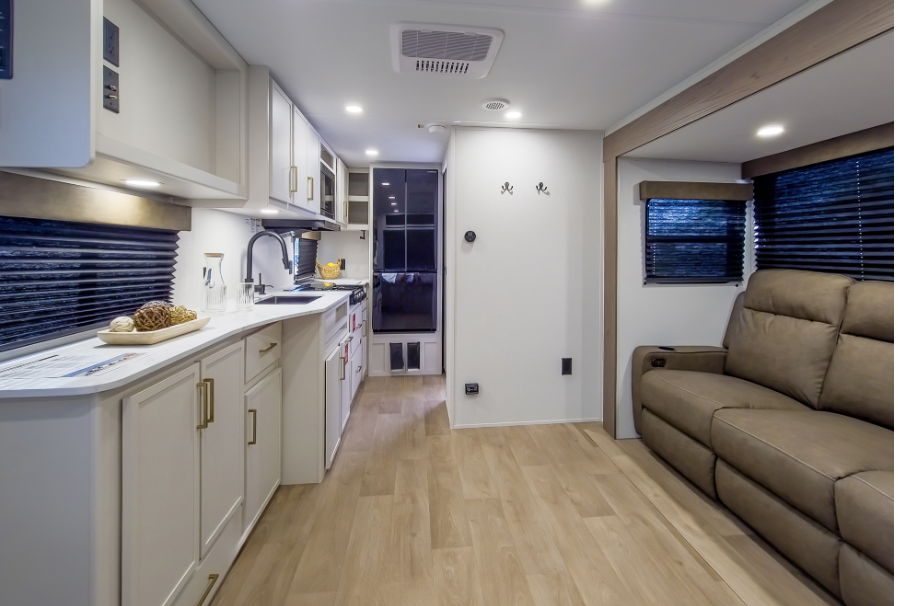 Travel trailer interior with full kitchen, white cabinetry, large sofa seating, and rear entry door.