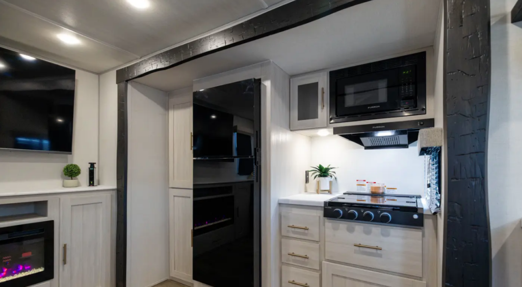 Travel trailer kitchen with gas range, microwave, large refrigerator, and entertainment center with electric fireplace.