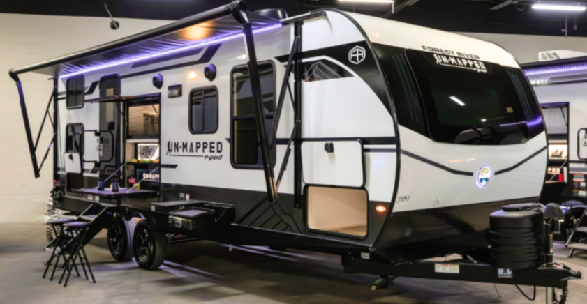 Forest River Unmapped R-Pod travel trailer with extended awning and outdoor kitchen displayed at an RV show.