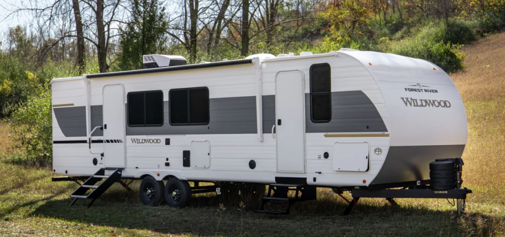 Forest River Wildwood travel trailer parked on a grassy hillside with slide-out extended and dual axles.