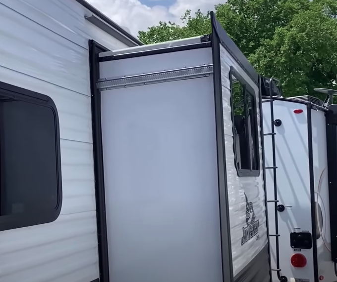Close-up of RV slide-out exterior extended from a travel trailer with ladder visible on the rear.