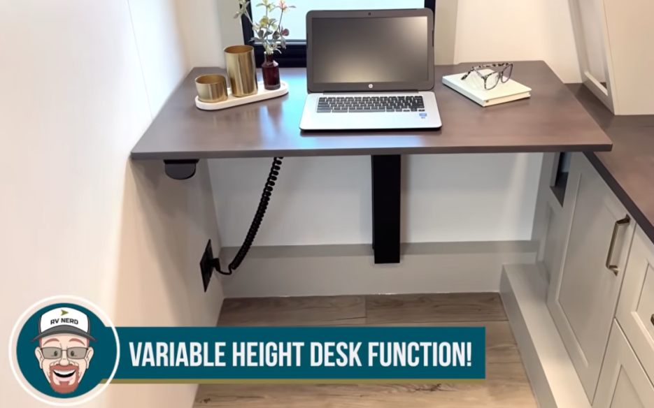 Adjustable height desk in a travel trailer with laptop and workspace setup, labeled variable height desk function.