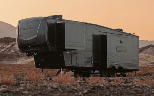 Keystone Cougar fifth wheel RV with slide-out extended parked in a rugged desert landscape at sunset.