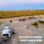 Aerial view of RV campground with multiple trailers and vehicles parked in a desert landscape at sunset.