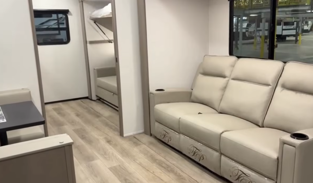 Spacious travel trailer interior with a light-colored sofa, wood-look flooring, and hallway leading to bunk beds in the rear.