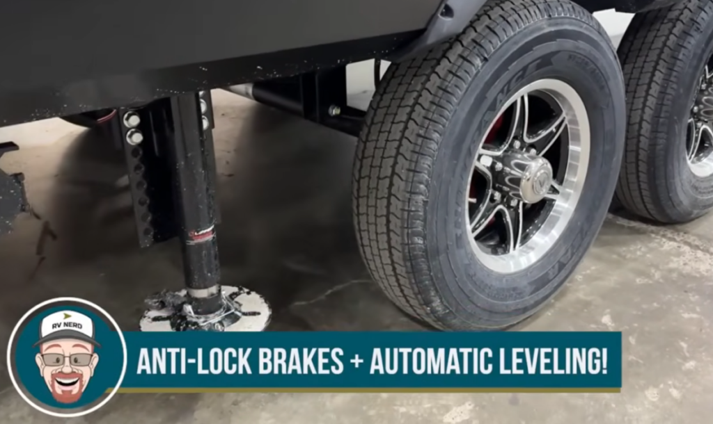 Close-up of a travel trailer’s wheels and stabilizer jack with text overlay reading “Anti-lock brakes + automatic leveling!
