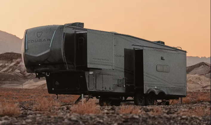 Fifth wheel RV parked in a desert landscape at sunset, with slide-out extended and rugged terrain in the background