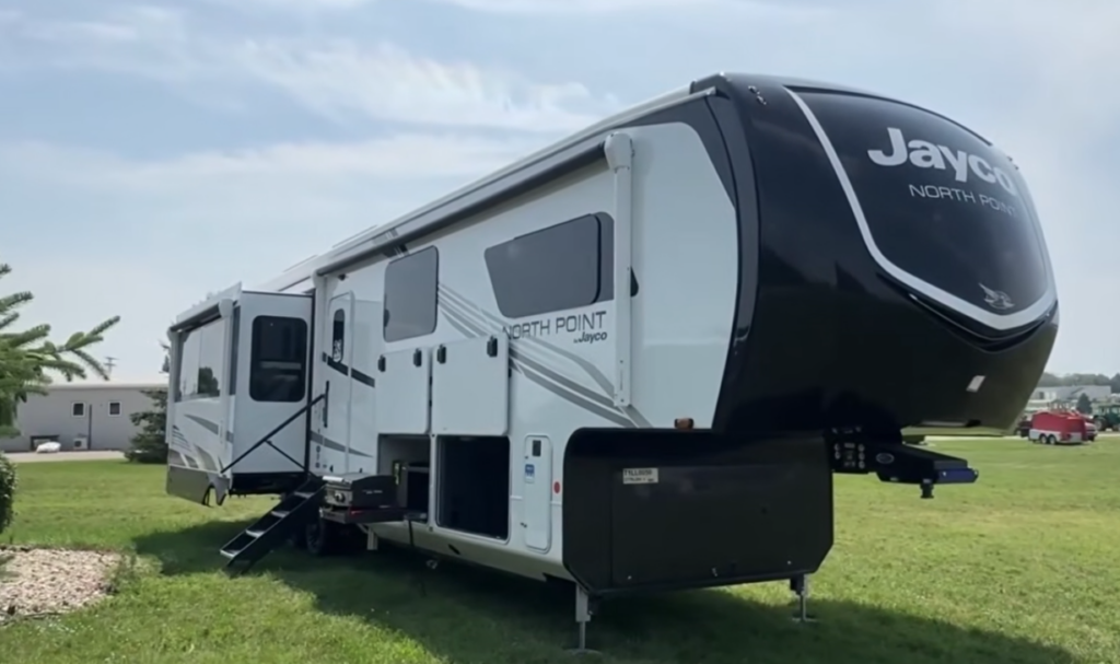 Jayco North Point fifth wheel RV parked on grass with slide-outs extended and front cap prominently visible.