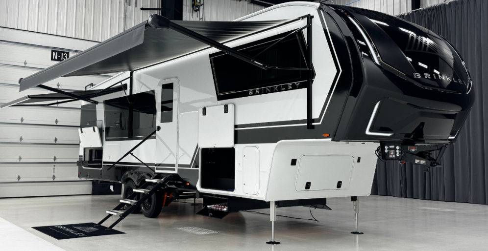 Brinkley fifth wheel RV displayed indoors with awning extended, storage compartments open, and front cap design prominently visible.