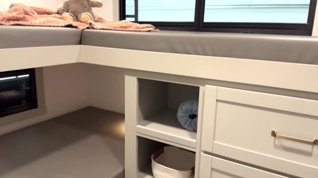 Travel trailer bunk area with elevated mattress, built-in shelving, storage drawers, and lower sleeping space beneath
