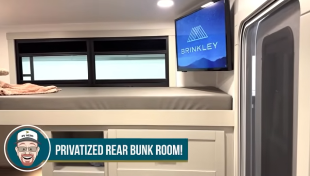 Travel trailer rear bunk room with elevated bed, storage drawers below, TV mounted on the wall, and text overlay reading “Privatized rear bunk room!