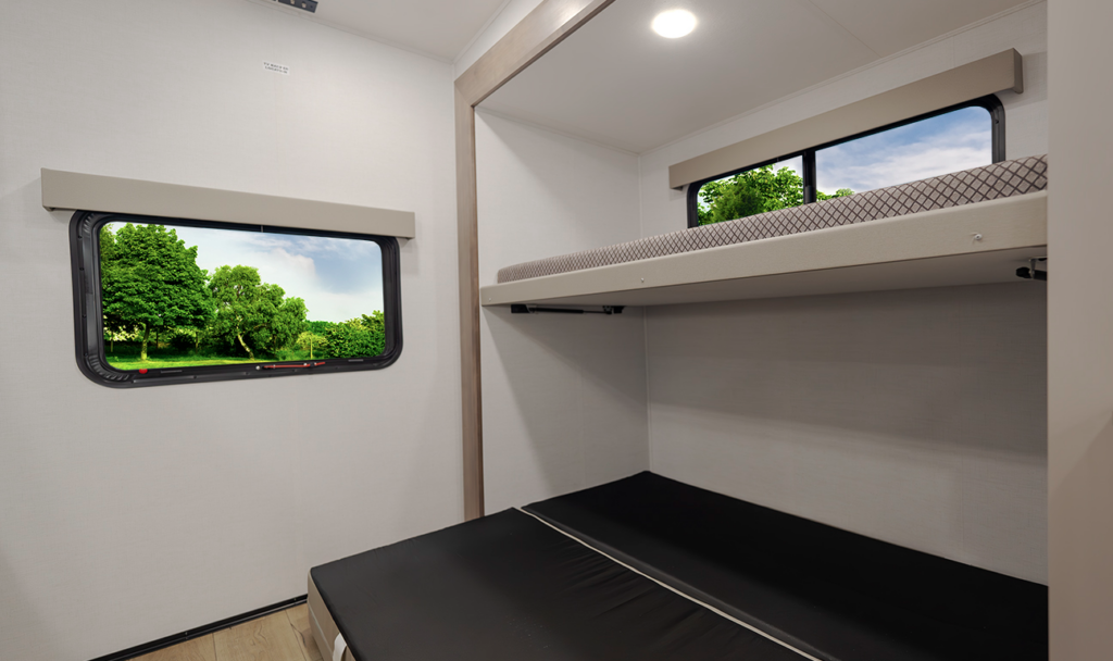 Travel trailer bunk room with an upper bunk, lower convertible sleeping area, and two windows offering outside views