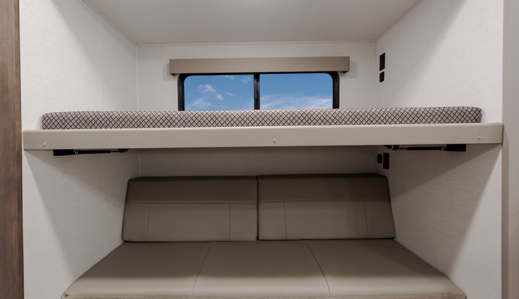 Travel trailer bunk room with an upper bunk and lower convertible sofa-style sleeping area, with a window centered above.