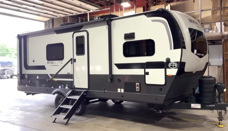 Rockwood Mini Lite travel trailer displayed indoors with entry steps down, front hitch visible, and exterior storage compartments along the side.