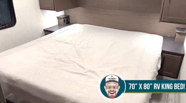 Travel trailer bedroom with a king-size bed (70" x 80"), side nightstands, and overhead cabinetry.