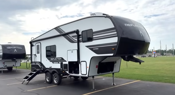 Grand Design Reflection fifth wheel RV parked on a lot with front hitch elevated, dual axles, and entry steps extended.