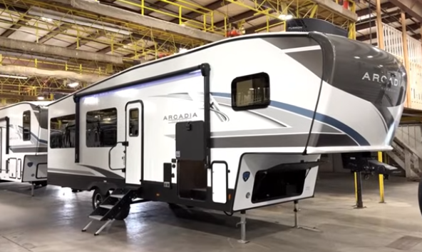 Arcadia fifth wheel RV displayed indoors with slide-out extended, entry steps down, and front hitch elevated.