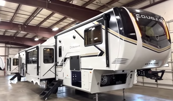 Keystone Cougar fifth wheel RV displayed indoors with slide-outs extended, entry steps down, and front hitch elevated.