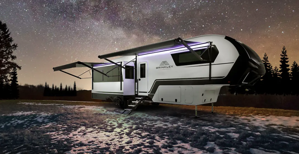 Brinkley fifth wheel RV set up at night under a star-filled sky with awning extended, exterior lights on, and steps leading up to the entrance.
