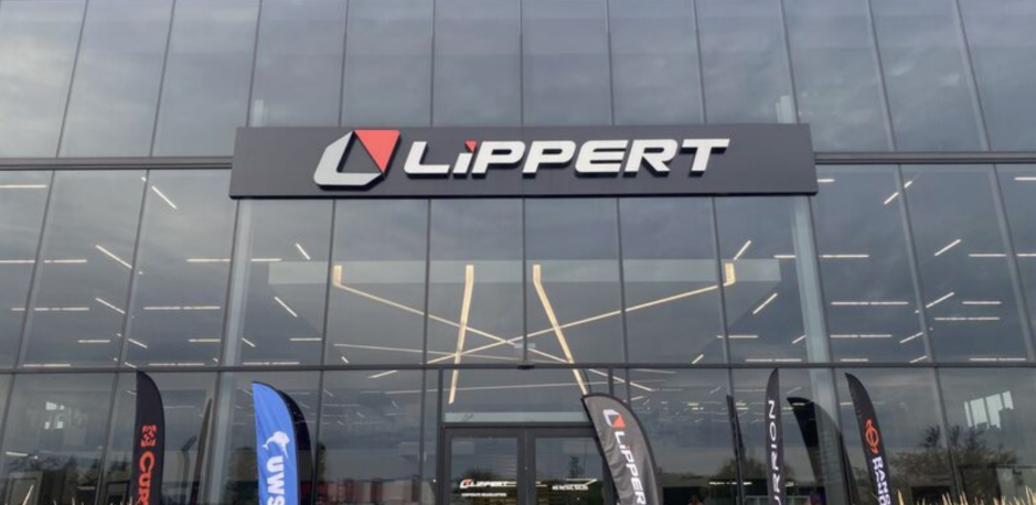 Exterior of a Lippert building with large glass windows, company signage above the entrance, and branded flags displayed outside.