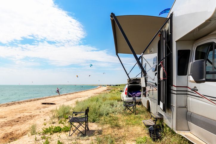 Panoramic view of many surf board kite riders on sand beach watersport spot on bright sunny day against rv camper van vehicle at sea ocean coast at surfing camp. Fun adventure travel sport acitivity.