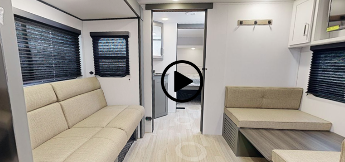 Compact RV interior with bench seating, dining table, blackout window shades, and hallway leading to the rear bedroom and bathroom.
