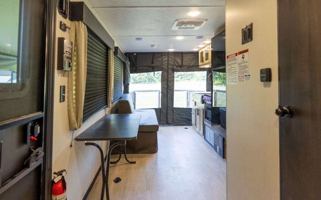 Pop-up style travel trailer interior with kitchenette, bench seating, folding table, blackout shades, and canvas tent extension at the rear