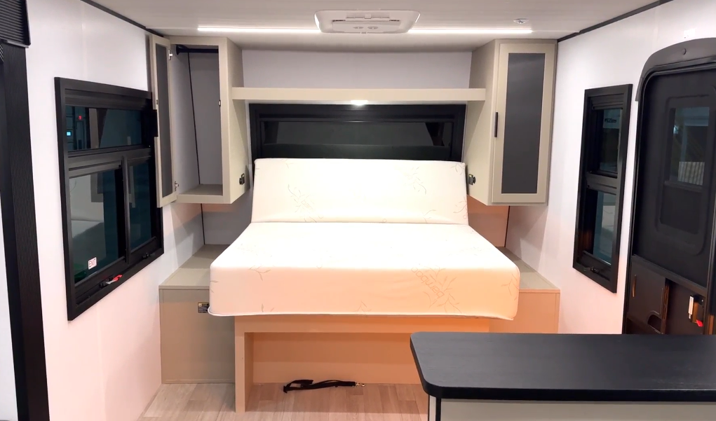RV interior featuring a fold-down Murphy bed with surrounding storage cabinets, side windows, and a small dining table in the foreground