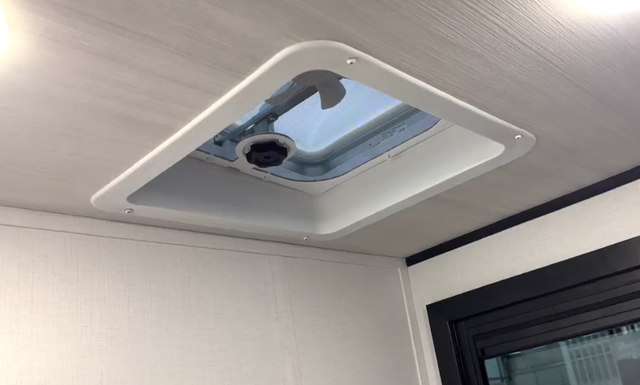 Close-up of an RV ceiling skylight vent with crank handle and surrounding trim.
