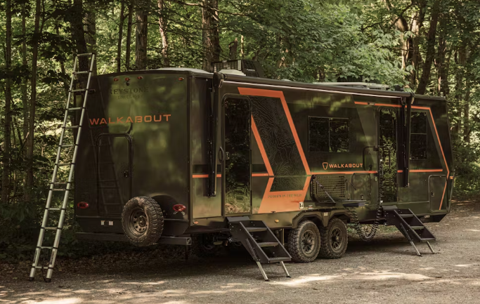 Keystone Walkabout travel trailer with black and orange exterior, dual entry doors, rooftop rack, and exterior ladder parked in a wooded campsite.