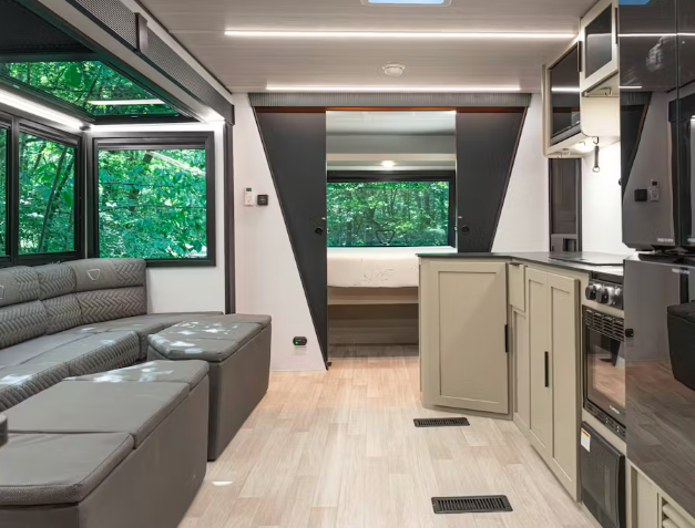 Modern bunkhouse RV interior with kitchenette, sofa seating, large windows, and stacked bunk beds with built-in ladder.