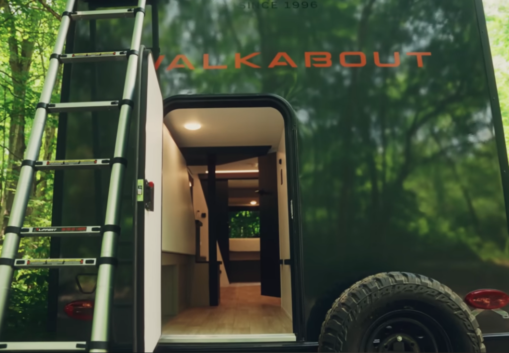 Rear entry of a Keystone Walkabout travel trailer with exterior ladder, spare tire, and open door revealing the interior.