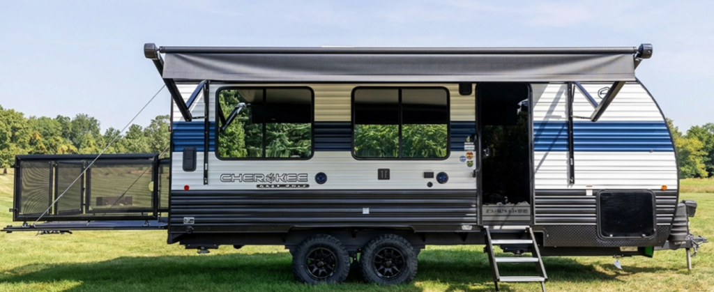 Cherokee travel trailer with blue and white exterior, extended awning, tandem axles, and rear fold-out patio deck parked on grass