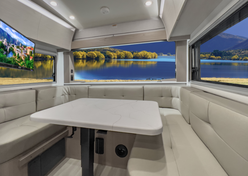 RV dinette lounge with wraparound seating, large panoramic windows overlooking a lake and mountains, and a modern center table