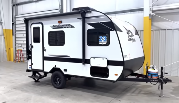 Compact Jayco Jay Feather Micro travel trailer with white exterior, black trim, single axle, and power awning displayed inside a warehouse