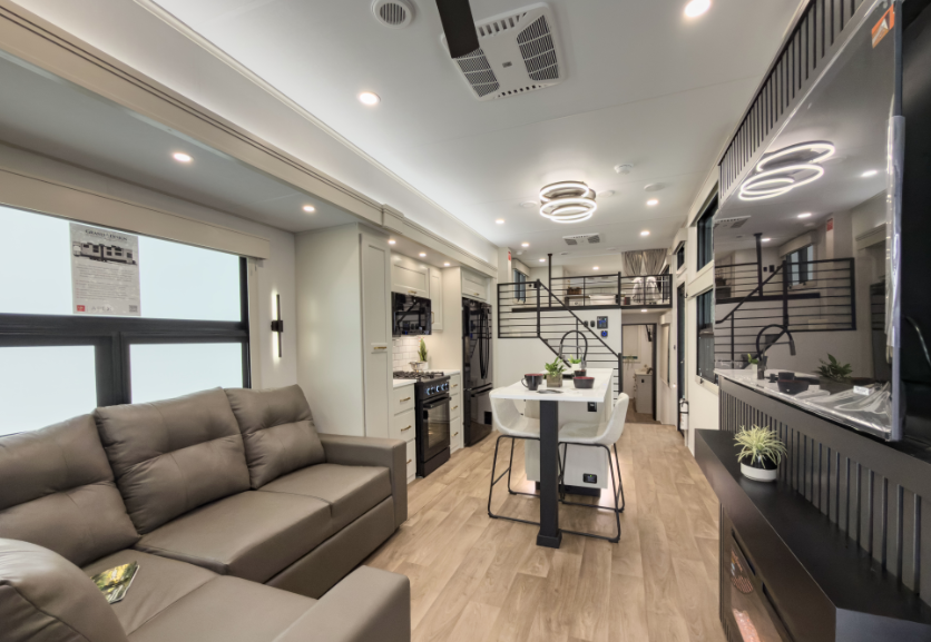 Luxury RV interior with residential-style living room, dining table, entertainment center, loft sleeping area, and modern kitchen finishes