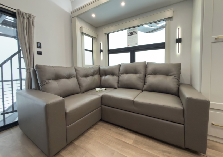 Modern RV living area with a plush L-shaped sectional sofa, large windows, and contemporary wall lighting beside a sliding glass patio door