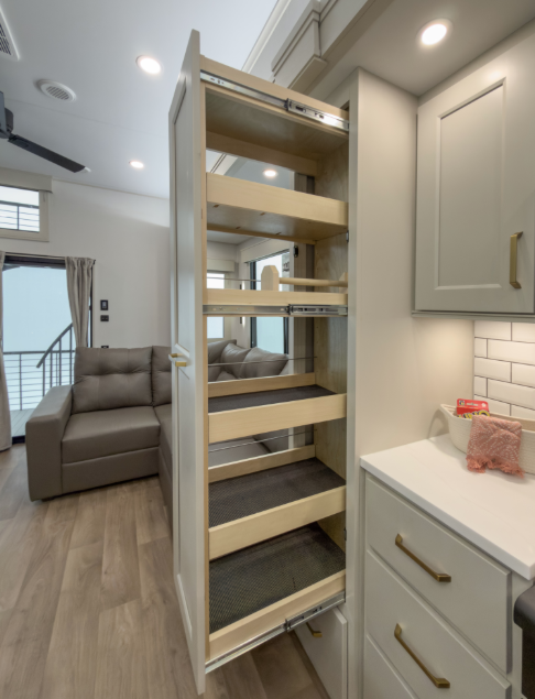 Luxury RV kitchen featuring a tall pull-out pantry cabinet with multiple storage shelves beside a residential-style cooking area.