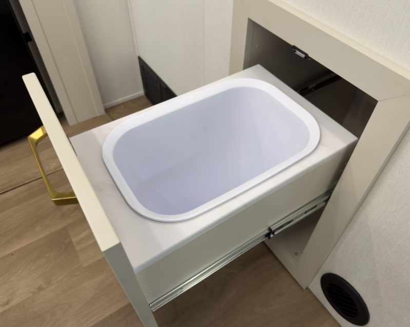 Hidden pull-out trash bin drawer integrated into a luxury RV kitchen cabinet with white finish and gold hardware