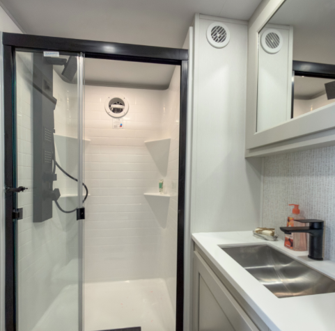 Modern RV bathroom with glass shower enclosure, black shower fixtures, white vanity countertop, stainless sink, and contemporary black faucet